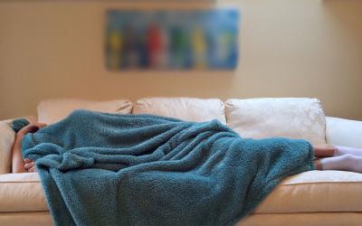 A person sleeping under a blue blanket on a white.