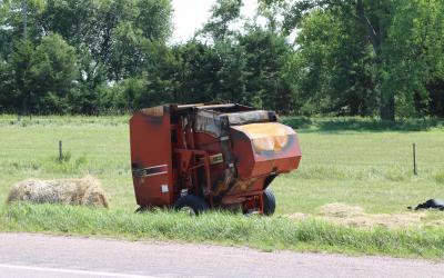 A red, round hay baler that has been burned up from a fire.