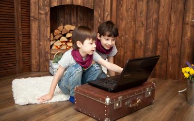 Two children sitting on the floor in front of a laptop. One of the children is pointing at the computer screen.