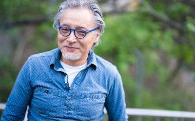 an older man with a blue shirt standing in front of some trees
