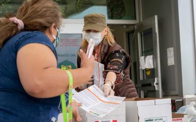 A local official wearing a mask handing a set of instructions to a woman also wearing a mask.