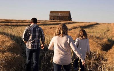 A father, mother and daughter walking in a field in the countryside.