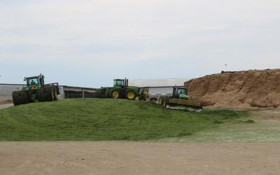 Three John Deere Tractors moving silage and packing the corn silage to make a drive over silage pile.