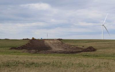 A dirt road leading to a winder energy station in the middle of a grassland area.