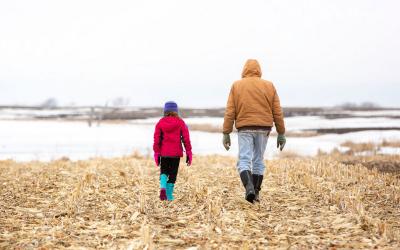 Young girl and grandfather walking through cornfiled stuble in winter.