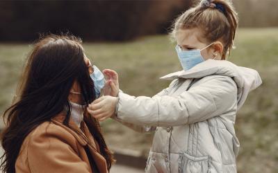 Mother and young daughter wearing masks in an outdoor park.