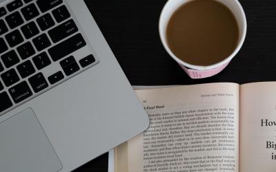 a laptop sitting next to a book and a cup of coffee
