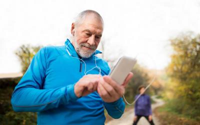 Older couple walking on a trail in the countryside. Husband is checking his activity tracker on his phone.