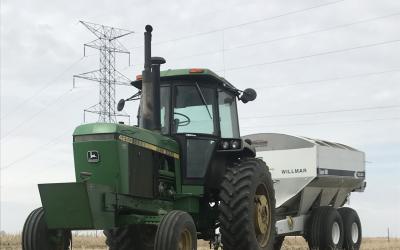 a green tractor pulling a white manure spreader in a field