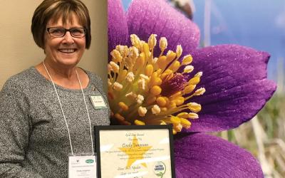Cindy Jungman holding an award in front of an SDSU Extension Master Gardener Program banner.