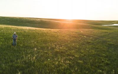 Rancher standing in a vast, rolling grassland.