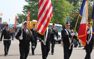 several older men in uniform marching while holding flags