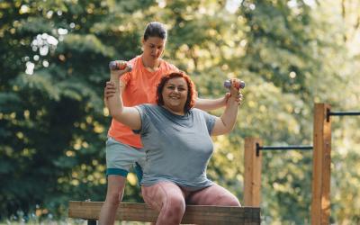 Female fitness instructor assisting an adult female at an outdoor gym.