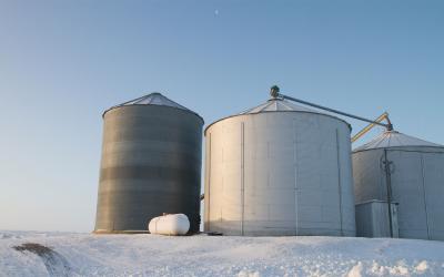 Three grain bins on the edge of a snow-covered field.