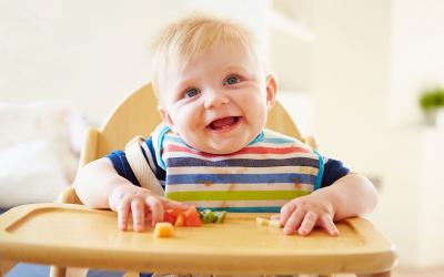 Baby seated at a highchair with a variety of soft, cut-up foods on its tray.