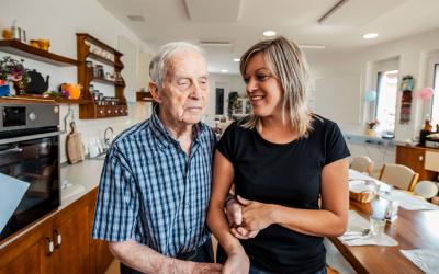 Older adult man getting assistance from a young, female caregiver.