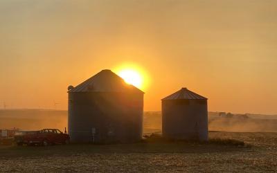 Sunset over two grain bins in a field.