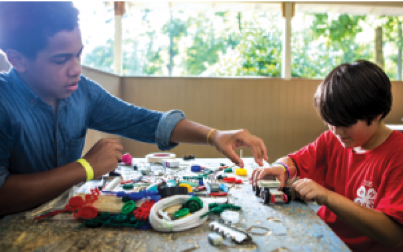Two young boys at a table constructing a robot.