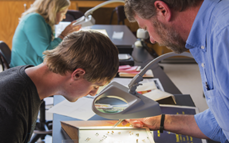 Teen boy and adult male reviewing specimens under magnifying glass.