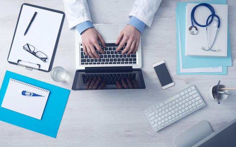 Doctor at laptop with insurance paperwork.