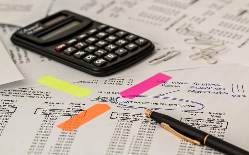 Calculator and pen sitting atop a bill