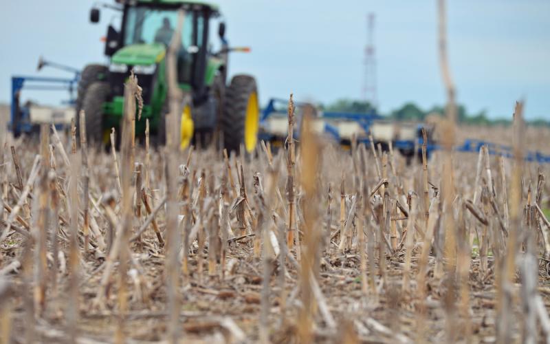 A green tractor planting soybeans in a field that's ready to plant.
