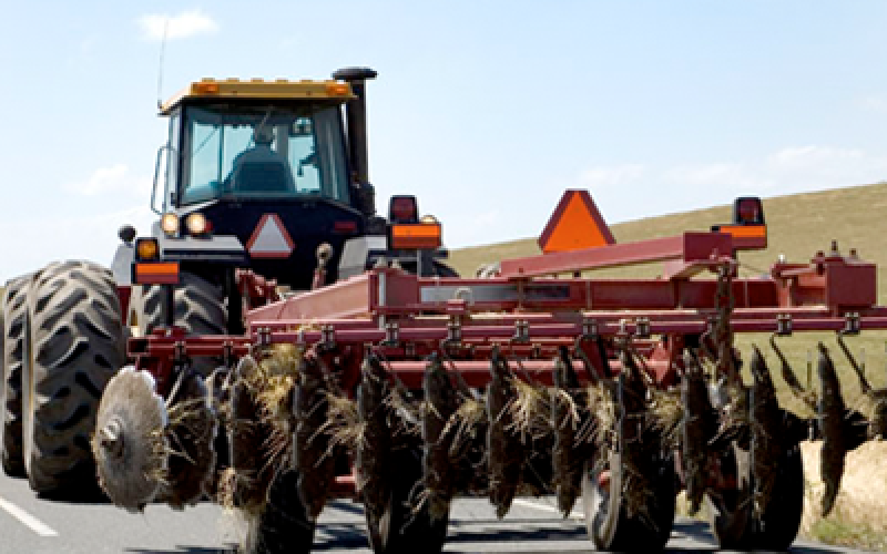 A red tractor driving on a county highway with an orange triangle sign on the rear.