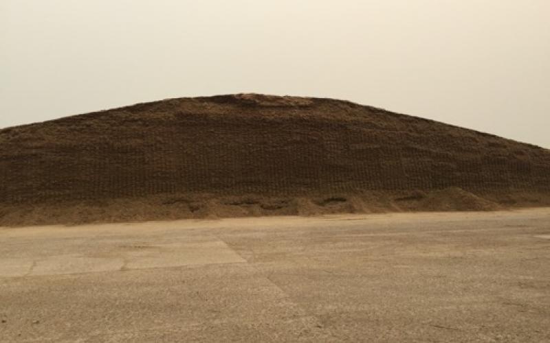A large pile of silage on a farm lot.