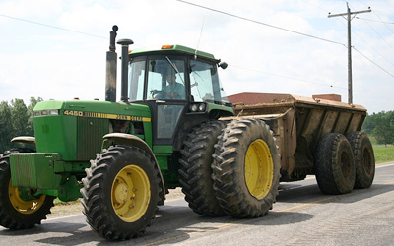 A green tractor pulling a feed wagon behind it on the road.