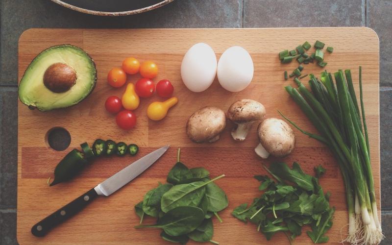 a wooden cutting board, a knife, and a frying pan with a variety of vegetables