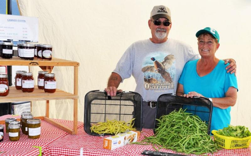 A husband and wife displaying fresh produce at a farmer's market stand.