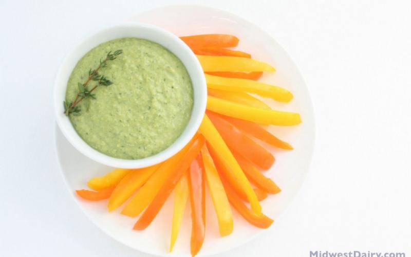 sliced orange and yellow peppers on a plate with green dip.