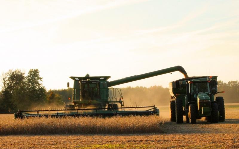 A combine harvesting soybeans and emptying them into a nearby tractor trailer