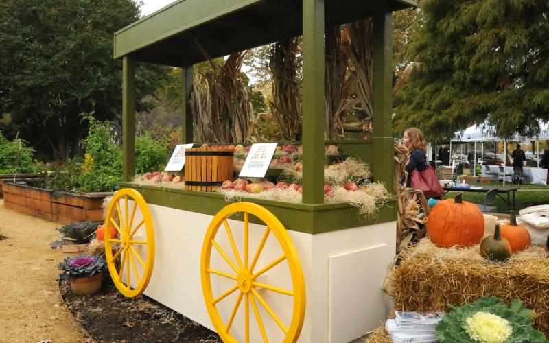 A produce stand with yellow wagon wheels and a green canopy.