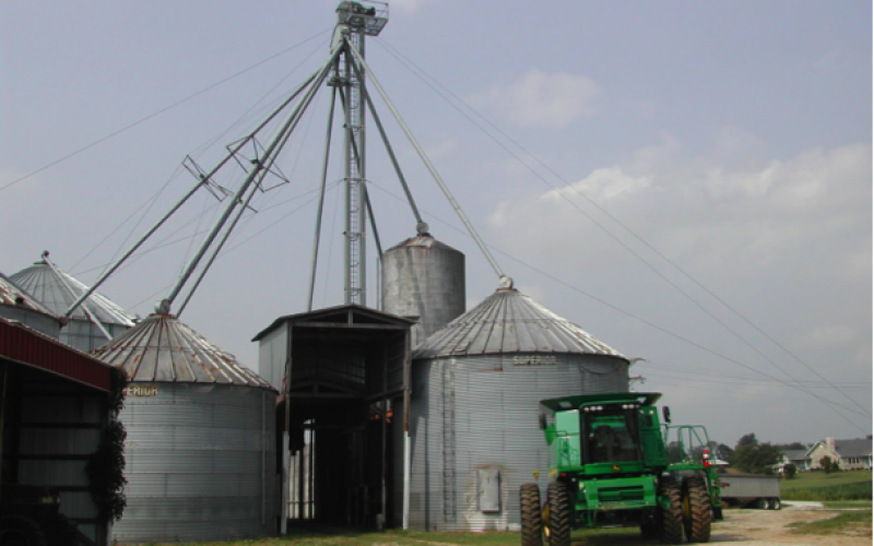 A group of grain bins with a green harvester in front.