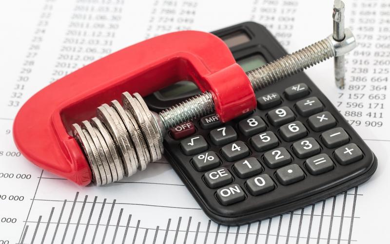 stack of coins in a vice atop a calculator representing a tight budget