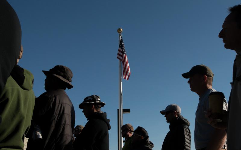A group of people watching a speaker. American flag in background.