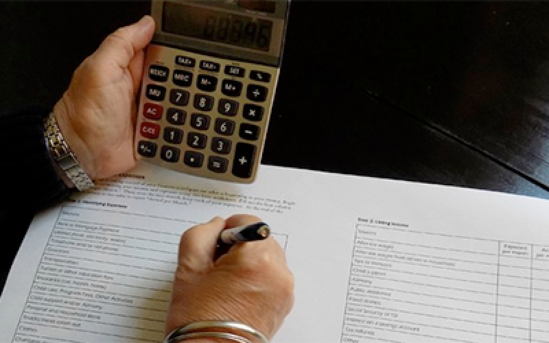 pair of hands reviewing a budget sheet with a calculator and pen