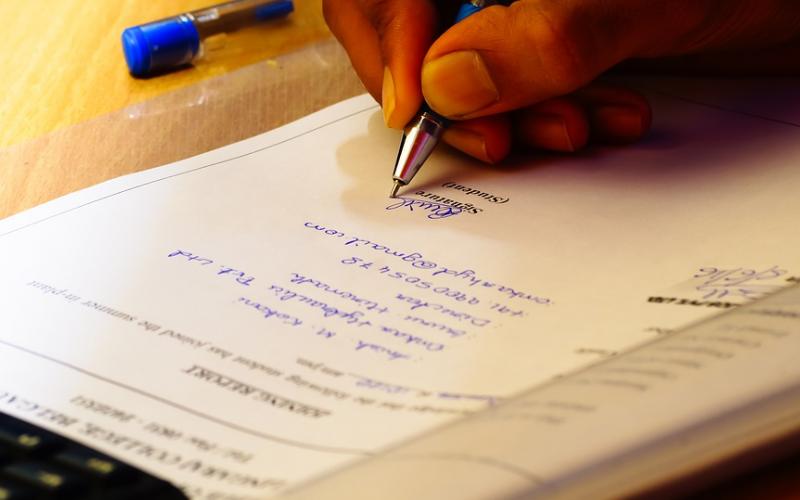 A hand writing on a financial document with a pen.