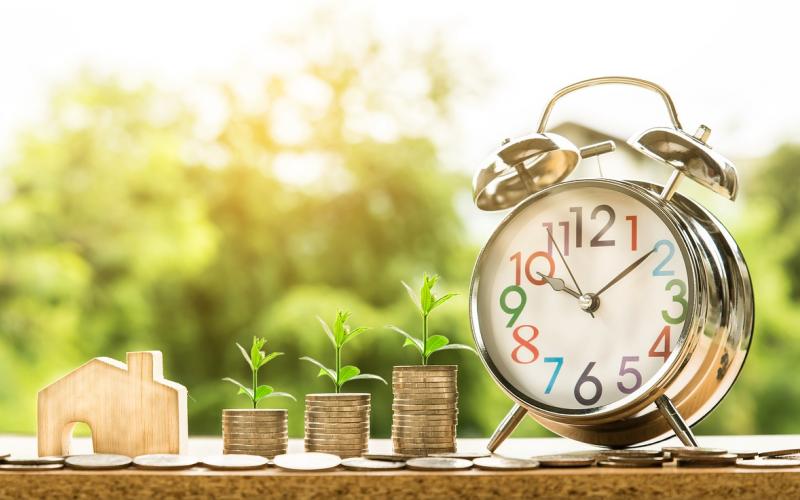 A house and tacks of coins with a clock representing savings growth.