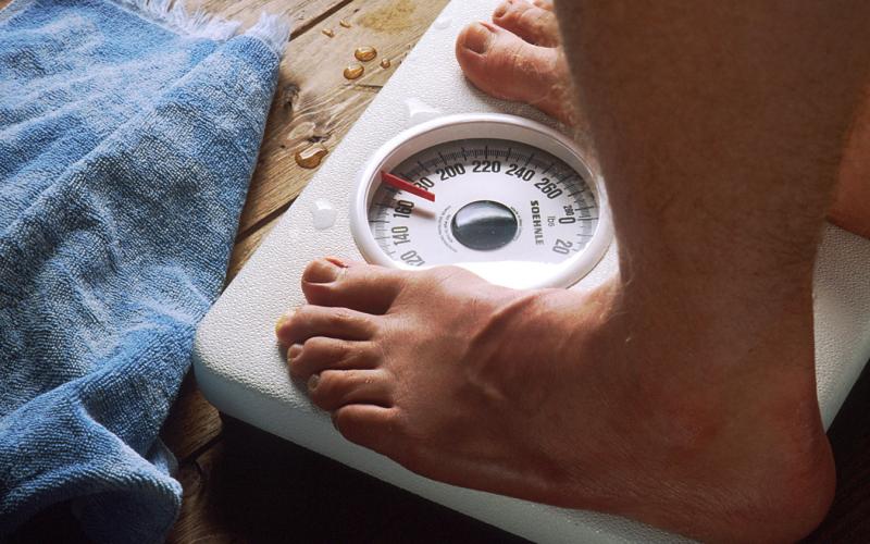 Close-up of the feet of a man standing on a bathroom scale with a blue towel lying nearby.