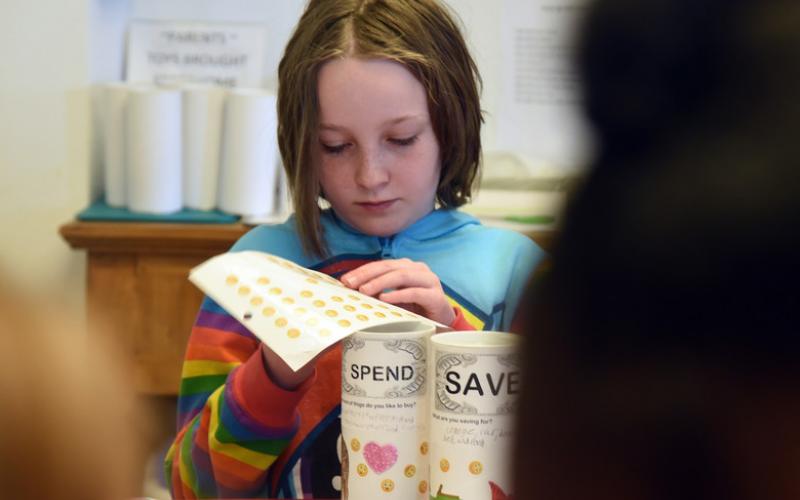 Young girl decorating two cans for saving and spending.