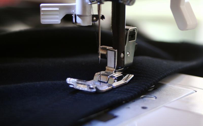 a sewing machine stitching a piece of navy blue fabric