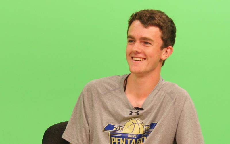 a teenage male sitting at a news desk in front of a green screen