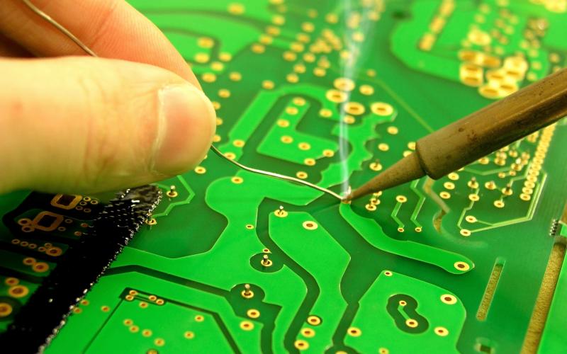 pair of hands soldering a green electronic circuit board