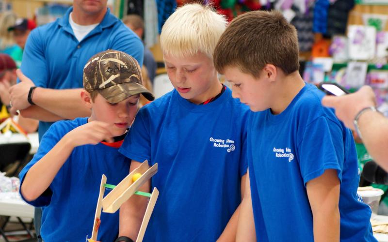 three male 4-H youth inspecting a catapult that they built