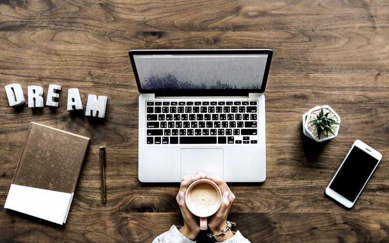 laptop, cell phone, and notebook sitting atop a brown, wooden desk.