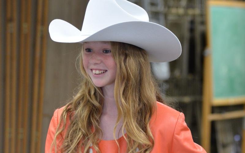 female 4-H youth wearing an orange western-style outfit with a white cowboy hat