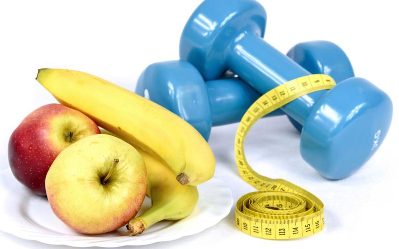 apples and bananas sitting on a plate next to a set of blue hand weights and a body measuring tape