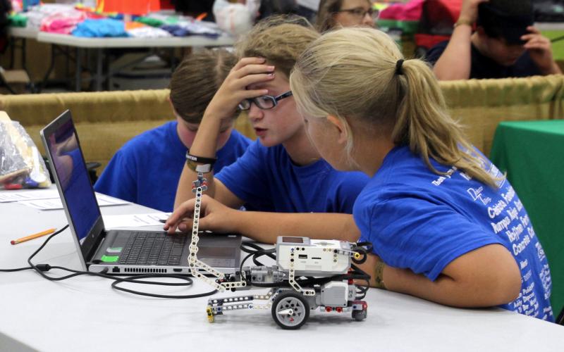 two male and one female 4-H youth inspecting a robotics control program on a laptop